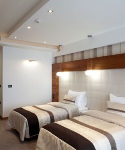 Διπλό κρεβάτι ξενοδοχείου με μοντέρνο φωτισμό και κομοδίνο, ιδανικό για άνετη διαμονή.