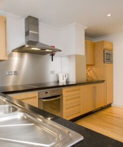 Σύγχρονη κουζίνα με ξύλινα ντουλάπια, ανοξείδωτο απορροφητήρα και εντοιχισμένες συσκευές.