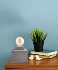 Διακόσμηση γραφείου με μοντέρνα λάμπα, συνθετικό φυτό και στοίβα βιβλίων πάνω σε ξύλινο τραπέζι.