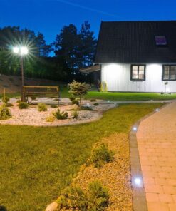 Εξωτερικός χώρος με φωτισμό κήπου και πλακόστρωτο μονοπάτι δίπλα σε εξοχικό σπίτι τη νύχτα.