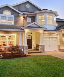 Διώροφο σπίτι παραδοσιακής αρχιτεκτονικής με φωτισμένες βεράντες και γκαράζ, καταξιωμένο στον κήπο.