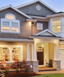 Σπίτι διώροφο με γκρι και λευκή όψη, κήπος μπροστά και ζεστός εξωτερικός φωτισμός.