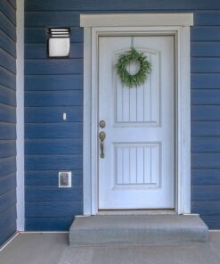 Φωτιστικό εξωτερικού χώρου σε φωτεινό λευκό και μαύρο, τοποθετημένο δίπλα σε λευκή εξώπορτα με γαλάζιο φόντο.